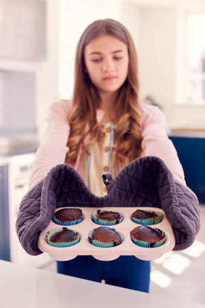Disappointed Teenage Girl Taking Out Tray Of Burnt Homemade Cupcakes From The Oven At Homeの写真素材