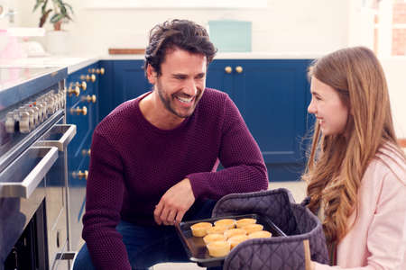 Father With Teenage Daughter Taking Out Freshly Baked Homemade Cupcakes From The Ovenの写真素材