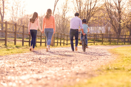 Rear View Of Family On Summer Walk In Countryside Teaching Son To Ride Bikeの写真素材