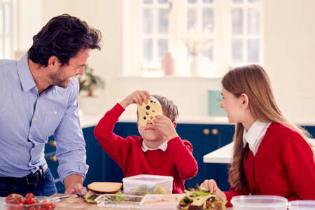 Father With Children Wearing School Uniform Having Fun Making Healthy Sandwich For Lunch At Homeの写真素材