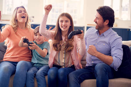 Parents Having Fun Sitting On Sofa With Children At Home Playing On Games Console