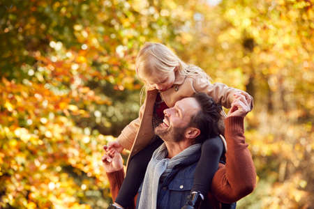 Father Playing Game Carrying Daughter On Shoulders On Family Walk Along Track In Autumn Countrysideの写真素材
