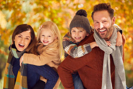Portrait Of Family With Parents Giving Children Piggybacks Against Autumn Leaves On Walkの写真素材