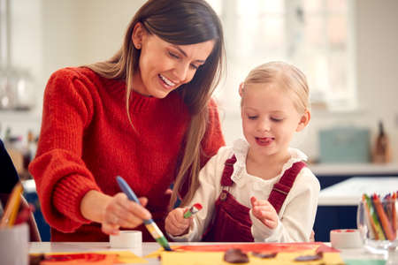 Mother With Daughter At Home Doing Craft And Painting Picture In Kitchenの写真素材