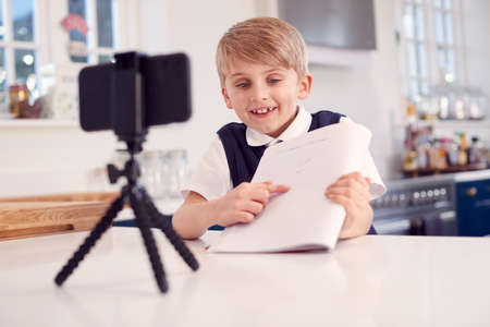 Boy At Home Wearing School Uniform Having Online Lesson Via Video Call On Mobile Phoneの写真素材