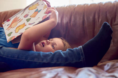 Close Up Of Father And Daughter Lying On Sofa At Home As Girl Reads Book