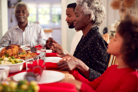Multi Generation Family Hold Hands Around Table At Home Saying Grace Before Eating Christmas Mealの写真素材