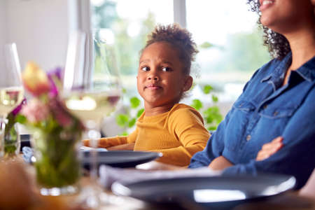 Mother And Daughter Sitting At Table Waiting For Multi-Generation Family Meal At Home