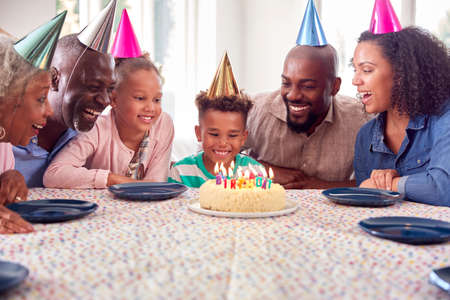 Multi Generation Family Sitting Around Table At Home Celebrating Boy's Birthday With Cake And Party