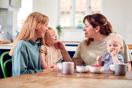 Two Mothers With Young Children Sitting Around Table On Play Date With Fruit Snacks