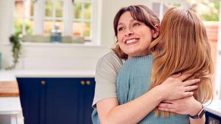 Two Female Friends Greeting And Hugging In Kitchen At Homeの写真素材