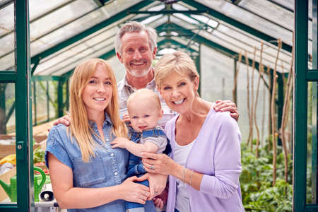Portrait Of Grandparents With Adult Daughter And Baby Grandson Standing In Doorway Of Greenhouseの写真素材