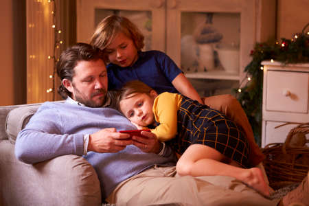 Father With Children In Armchair Playing Game Or Streaming On Mobile Phoneの写真素材