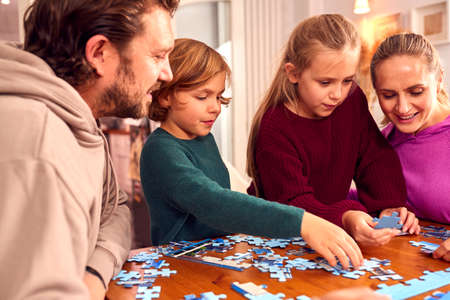 Family Sitting Around Table At Home Doing Jigsaw Puzzle Togetherの写真素材