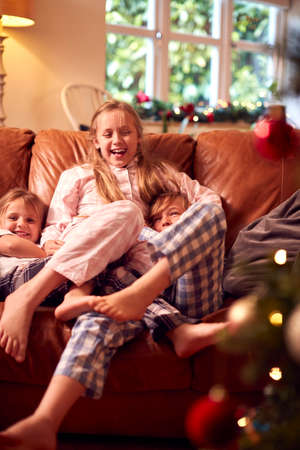 Three Children Wearing Pyjamas Opening Gifts Around Christmas Tree At Homeの写真素材