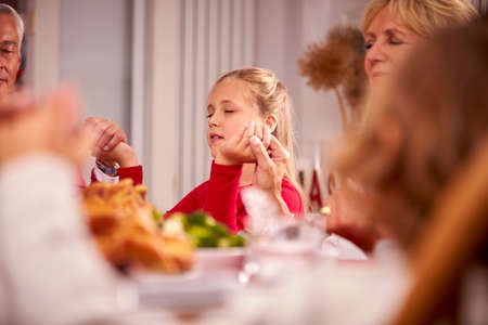Multi Generation Family Hold Hands Around Table At Home Saying Grace Before Eating Christmas Mealの写真素材