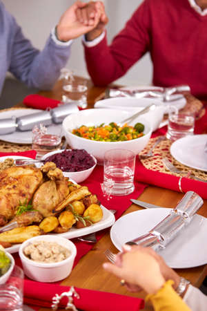 Multi Generation Family Hold Hands Around Table At Home Saying Grace Before Eating Christmas Mealの写真素材