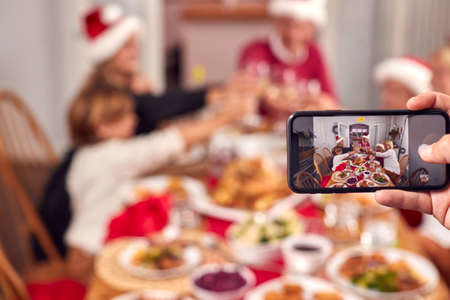 POV Shot Of Person Taking Photo Of Multi-Generation Family Meal At Christmas On Mobile Phoneの写真素材