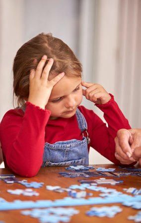 Close Up Of Granddaughter With Grandmother Sitting Around Table At Home Doing Jigsaw Puzzle Togetherの写真素材