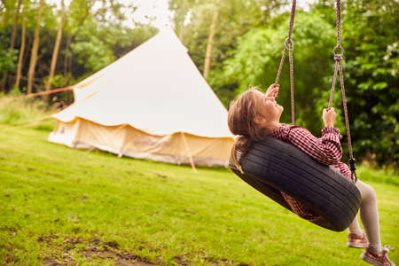 Girl Playing On Tyre Swing In Garden At Home With Tent In Backgroundの写真素材