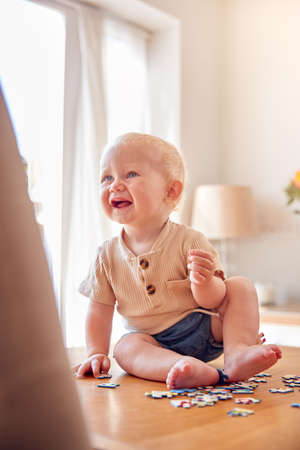 Laughing Baby Boy Having Fun Sitting At Home And Playing With Jigsaw Puzzle Piecesの写真素材