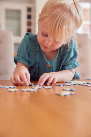 Young Girl Having Fun Sitting At Table At Home Doing Jigsaw Puzzleの写真素材