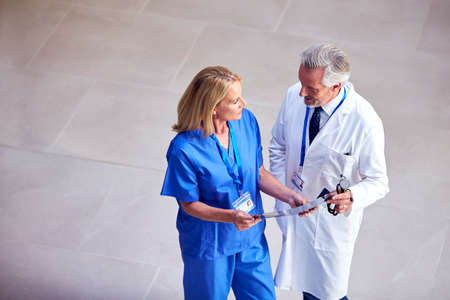 Overhead Shot Of Male Doctor Wearing White Coat Discussing Scan With Female Colleague In Scrubs