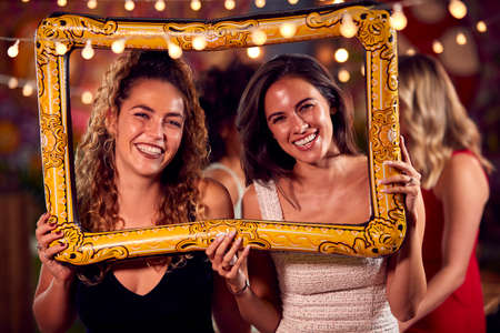 Female Friends Having Fun Posing With Photo Booth Photo Frame At Party In Barの写真素材