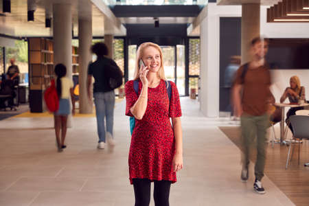 Female Student Talks On Mobile Phone As She Walks Through Busy University Or College Building