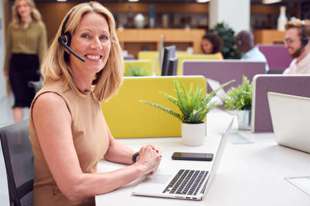 Portrait Of Mature Businesswoman Wearing Phone Headset Talking To Caller In Customer Services Centreの写真素材