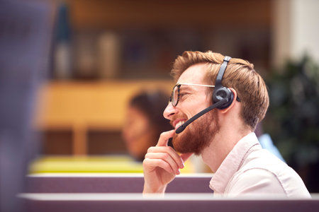Businessman In Cubicle Wearing Headset Talking To Caller In Busy Customer Services Centreの写真素材