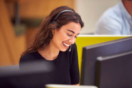 Businesswoman In Cubicle Wearing Headset Talking To Caller In Busy Customer Services Centreの写真素材