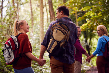 Rear View Of Mature And Mid Adult Couples In Countryside Hiking Along Path Through Forest Together