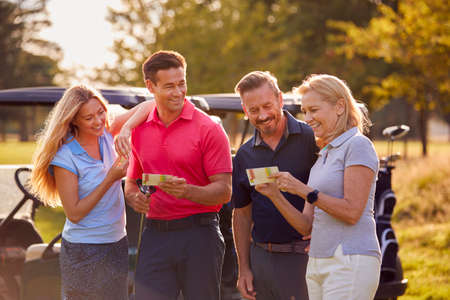 Mature And Mid Adult Couples Standing By Golf Buggy Checking Score Cards Together