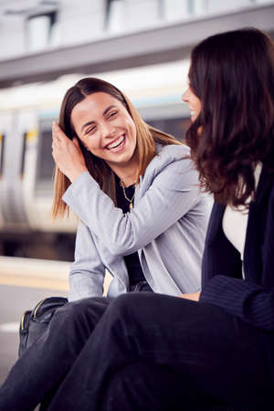 Two Businesswomen Commuting To Work Waiting For Train On Station Platform Talking Togetherの写真素材