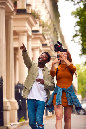 Young Couple Travelling Through City Together Vlogging To Video Camera On Handheld Tripodの写真素材