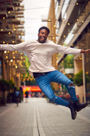 Portrait Of Young Man Enjoying City Life Jumping In Air Heading For Night Out