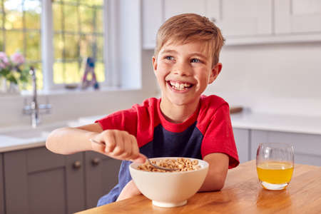 Boy At Home Eating Bowl Of Breakfast Cereal At Kitchen Counterの写真素材