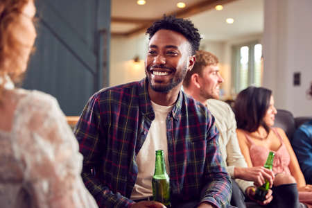 Young Couple Sitting On Sofa At Home Talking And Enjoying Drinks Togetherの写真素材