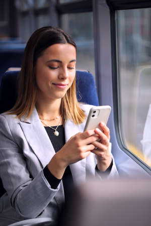 Businesswoman Commuting To Work On Train Looking At Mobile Phoneの写真素材