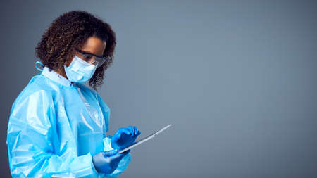 Studio Portrait Of Female Lab Worker in PPE With Face Mask And Safety Glasses Holding Digital Tabletの写真素材