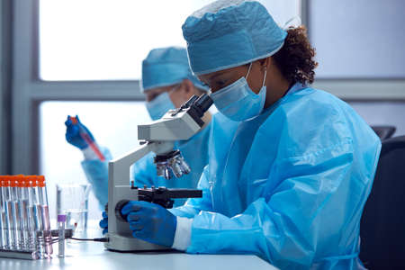 Female Lab Workers Wearing PPE Researching In Laboratory With Microscope