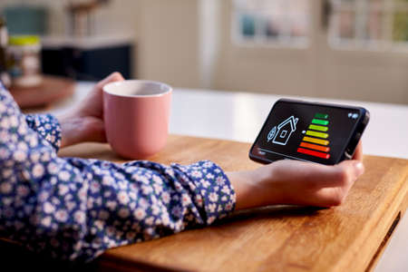 Close Up Of Woman Holding Smart Energy Meter In Kitchen Measuring Energy Efficiencyの写真素材