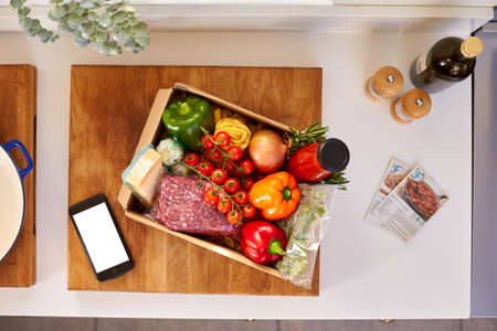 Overhead Of Phone With Recipe Cards By Box From Online Meal Food Recipe Kit Delivered To Homeの写真素材