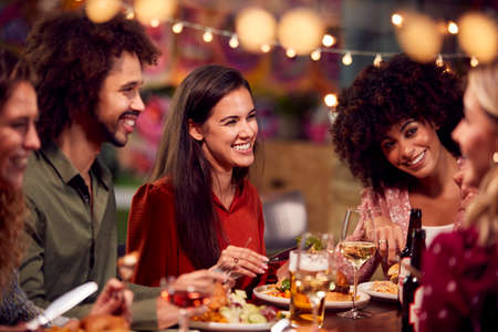 Multi-Cultural Group Of Friends Enjoying Night Out Eating Meal And Drinking In Restaurant Together