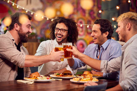 Multi-Cultural Group Of Male Friends Enjoying Night Out Eating Meal And Drinking In Restaurantの写真素材