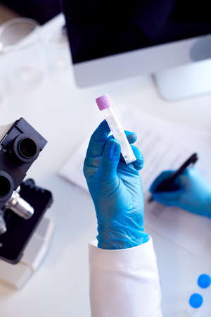 Close Up Of Lab Worker Conducting Research Using Microscope Holding Tube With PCR Test Swabの写真素材