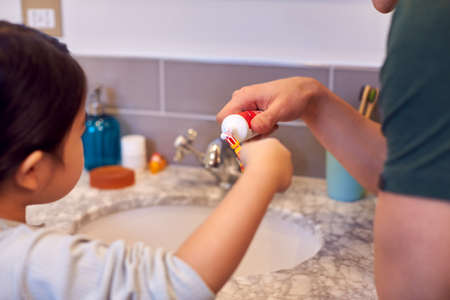 Family With Dad Helping Daughter With Toothpaste As She Brushes Teeth In Bathroomの写真素材