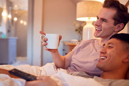 Loving Same Sex Male Couple Lying In Bed At Home Watching TV Togetherの写真素材