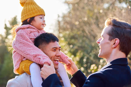 Family With Two Dads On Walk In Winter Countryside Carrying Daughter On Shouldersの写真素材